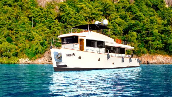 Trawler yat Maske 3, yemyeşil doğa manzarası önünde demirlemiş durumda.