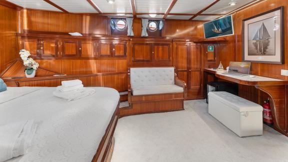 A spacious and luxurious cabin on board the Gulet Smart Spirit, with a large bed, a seating area and elegant wooden furn