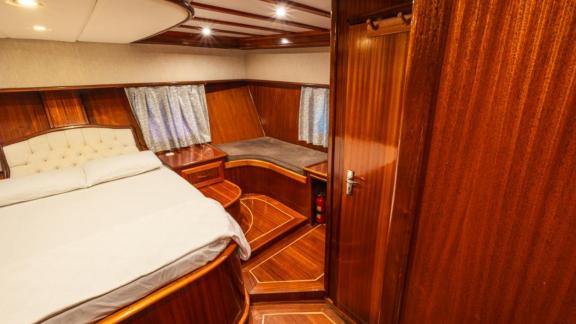 Master cabin of Gulet Esperanza featuring a central double bed, surrounding wood paneling, and a side bench.