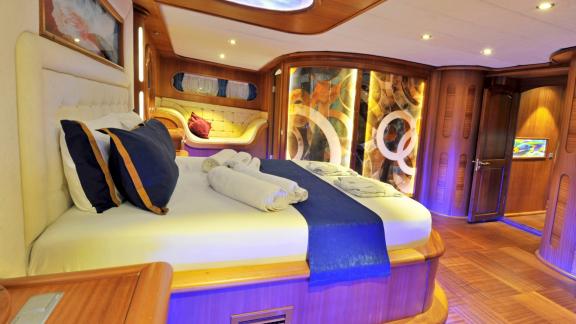 Large decorated bed, elegant wooden decor, and cozy sitting area in the yacht's bedroom