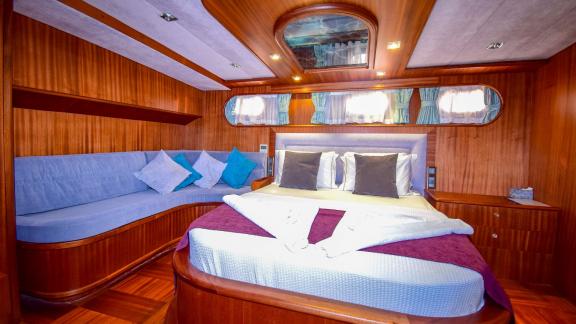 A cosy cabin on the gulet 'Ugur' with a large bed, sofa and wood panelling.