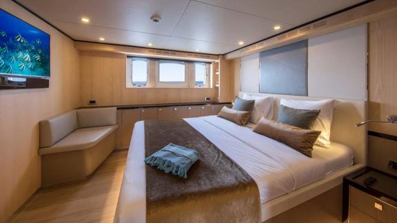 Helle Kabine mit Doppelbett, TV und Fensterblick auf See in der Sea Story Yacht.