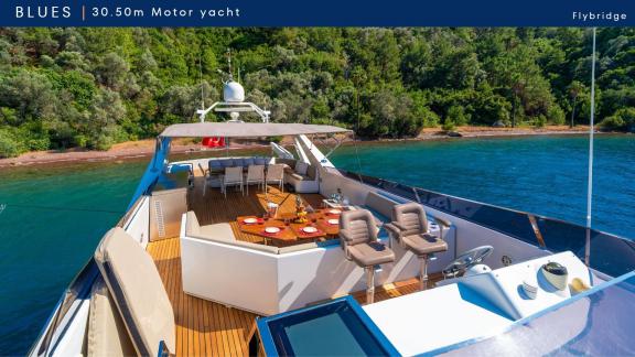 Blues motoryat flybridge alanında masa donatılmış. Yat ormanlık kıyıya yakın bir koyda demirli.