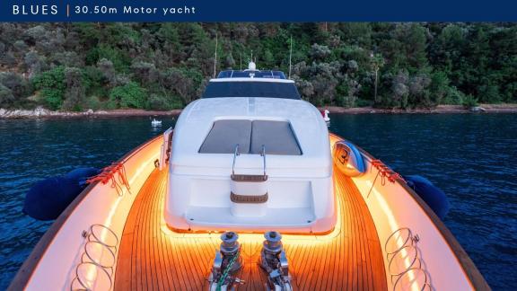 Blues motoryat ön güvertesi aydınlatılmış şekilde kıyıya yakın bir koyda demirlemiş.