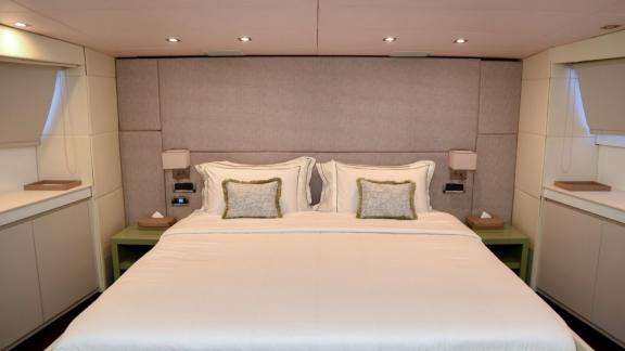 The master cabin of yacht Brooklyn offers a spacious bed, elegant grey headboard, and minimalist design for a modern and