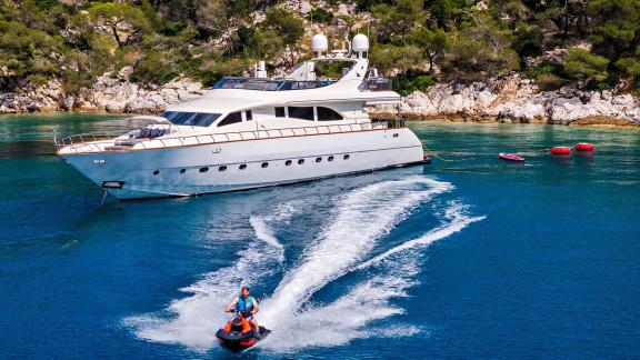 Dream motor yacht anchored in Athens bay as a jet ski rides fast across the water.