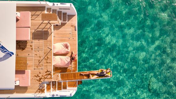 Anchored in Lavrion the 3 cabin 6 guest Omikron Yachts OT 60 N ice shows aft deck platform with sun lounger by the sea.
