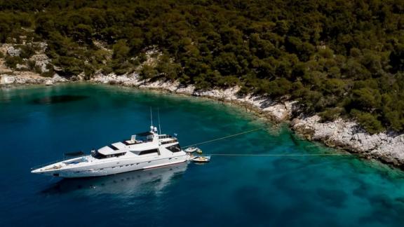 Wish Alfamarine 91 motor yacht is anchored in a turquoise bay, secured to shore with forested coastline behind.