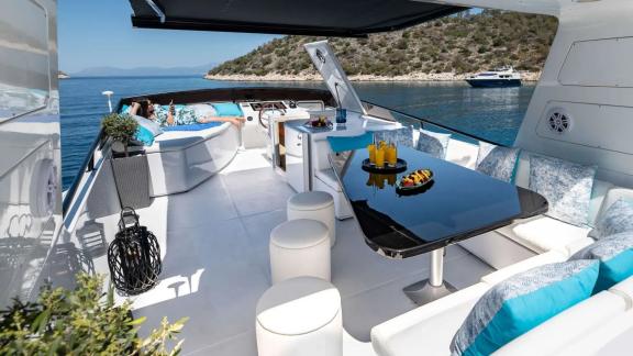 The flybridge of Wish Alfamarine 91 features seating areas, a table and a bay view in the background.