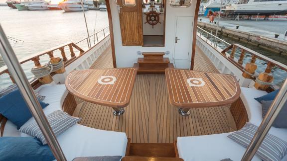 The aft deck of Cosmos features two wooden tables and cushioned seating.