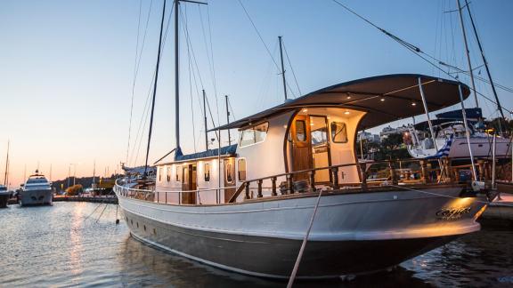 The motorsailer Cosmos is docked with its lights on at sunset.