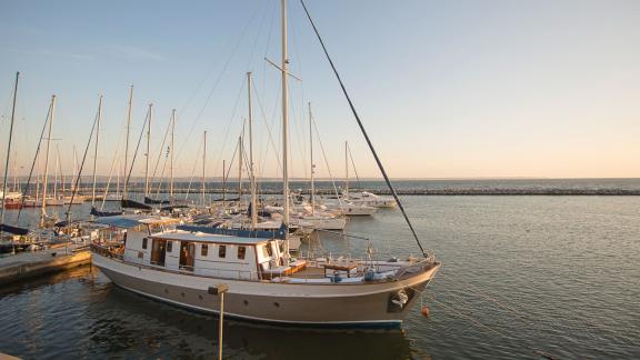The motorsailer Cosmos is anchored in the marina at sunset, surrounded by other boats.