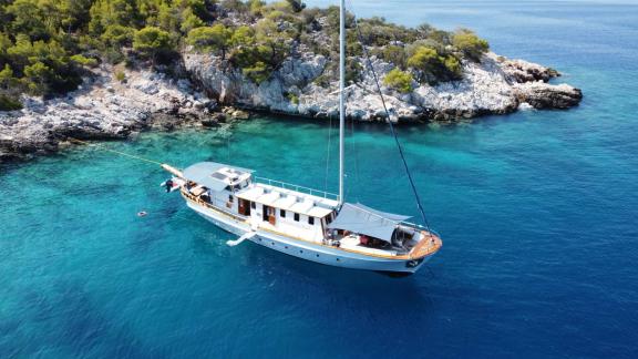 Cosmos is anchored in crystal-clear waters with a rocky, green island in the background.