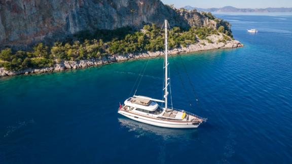 Eine 28 Meter lange Gulet ankert vor einer grünen, felsigen Küste in Göcek.