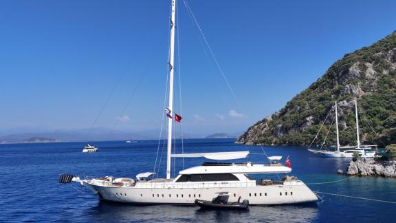 Anchored in Fethiye bay the 6 cabin 12 guest Dodo motorsailer seen from side with spacious deck and tender.