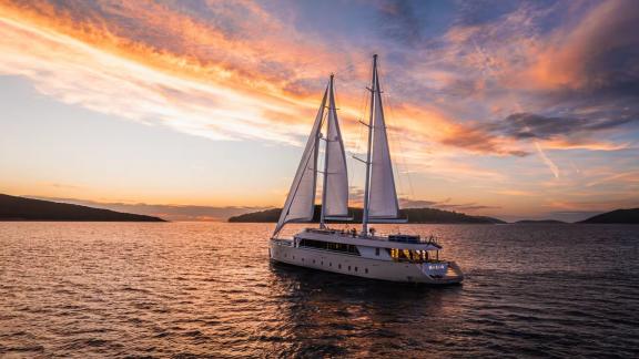 In Split motorsailer charter option Maxita sailing at sunset with sails open on calm sea.
