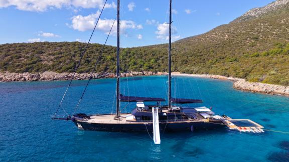 Oguz Khan моторсейлер стоит на якоре в бирюзовой бухте Бодрума просторная палуба и платформа для купания аренда яхты на