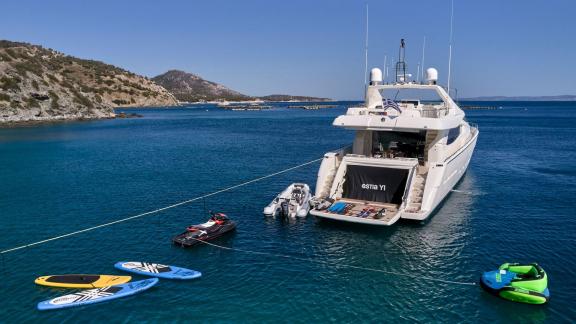 Luxurious motor yacht in a calm bay, surrounded by jet skis and paddleboards.