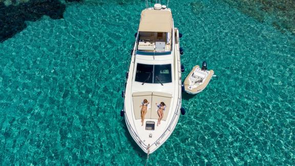 Die Motoryacht Free Day liegt in türkisfarbenem Wasser, Gäste sonnen sich auf dem Deck. Nebenan ein kleines Boot.