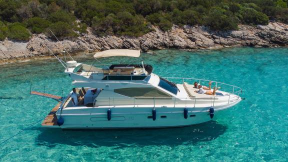 Die Motoryacht Free Day liegt in einer Bucht vor Anker, Gäste sonnen sich auf dem Deck. Rundherum klares türkisfarbenes 