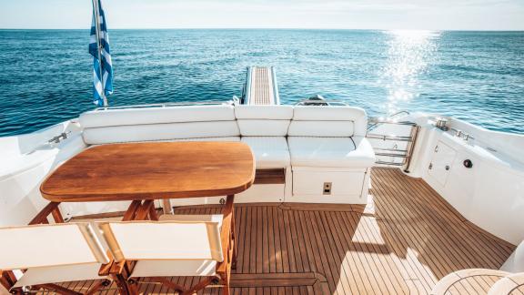 The aft deck of the Funseeker yacht features a wooden table and white seating with a sea view.
