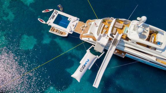 Die Yacht liegt ruhig mit Pool, Rutsche und Boards im klaren Wasser vor Anker.