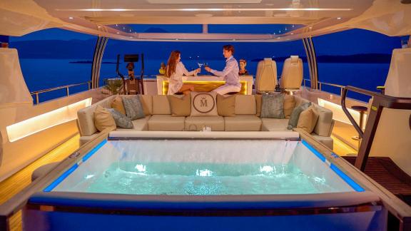 Auf der Princess 40M genießen Gäste Drinks bei beleuchtetem Jacuzzi und Aussicht.