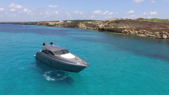 Die Yacht Optimum liegt still. Ihr grauer Rumpf und sportliches Design spiegeln sich im türkisfarbenen Meer.