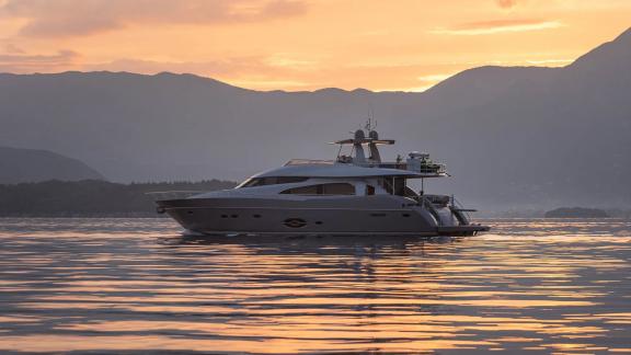 Stela 117 yacht glides on calm waters at sunset with mountains in the backdrop.