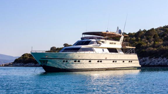 Sveti Sky motor yacht is anchored on calm waters with green hills rising in the background.