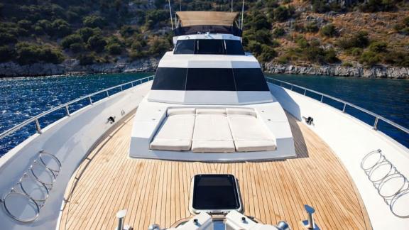 The foredeck of Sveti Sky features a large cushioned sunbathing area surrounded by turquoise waters.