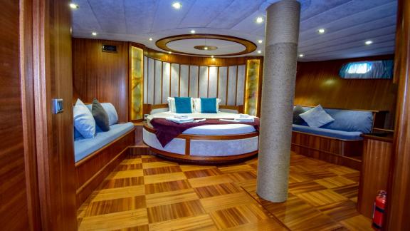 A spacious cabin on the gulet 'Ugur' with a round bed, seating and wood panelling.