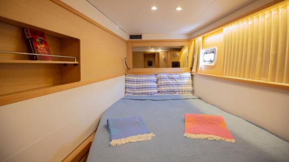 A cozy cabin on a Lagoon 560 catamaran in Göcek, featuring a double bed, a small shelf, and soft lighting, creating a re