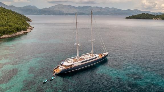 The Motor Sailor Nocturno anchored in clear waters with views of wooded shores and distant mountains.