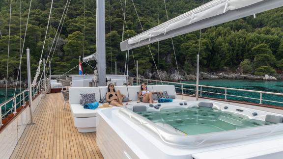 Two women relaxing in the hot tub on Nocturno's deck with a green coastline in the background.