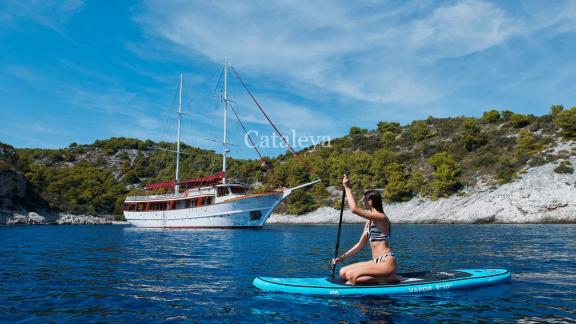 Gulet Cataleya with 9 cabins anchors in an idyllic bay in Croatia while a woman paddles on a SUP board.