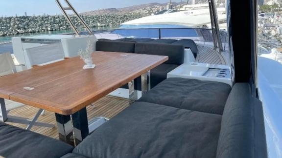 Cozy dining area with a wooden table and cushioned seating on the flybridge of Lagoon 630 Pearly Gates in Lavrion harbor