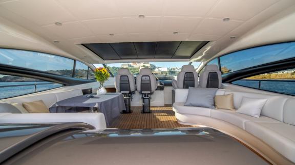 Im Innenbereich der Yacht befinden sich große Fenster und ein Ecksofa. Der Tisch ist mit Blumen dekoriert.
