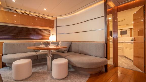 Die untere Lounge der Yacht bietet einen runden Tisch, graue Polster und Teppich. Sanftes Licht sorgt für Gemütlichkeit.