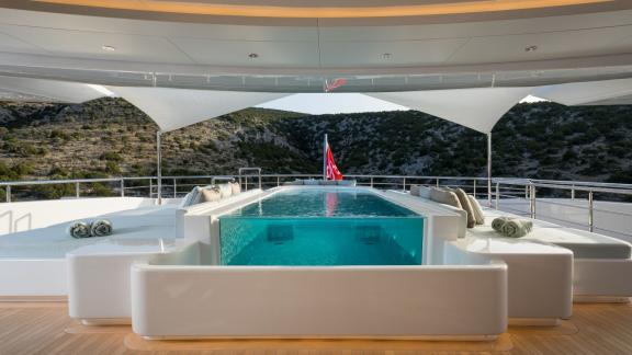 Breathtaking infinity pool on a luxurious yacht, surrounded by white loungers. View of hills and bay.