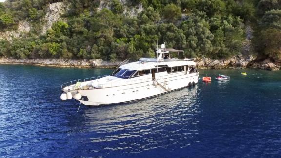 Die Motoryacht Samocla liegt vor Anker in einer ruhigen Bucht, umgeben von grünen Bäumen und klarem blauen Wasser.