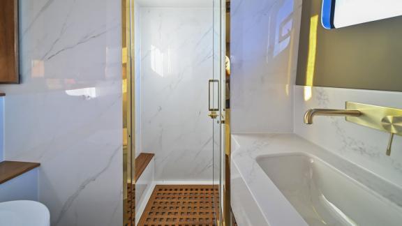 Evita power catamaran features a marble-finished shower cabin with glass door and wooden floor details.