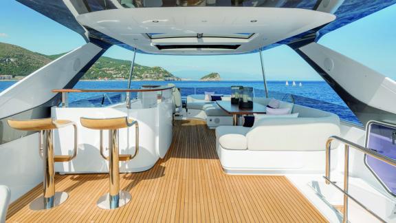 Stylish yacht lounge with bar and seating area, offering a wide view of the sea and coast.