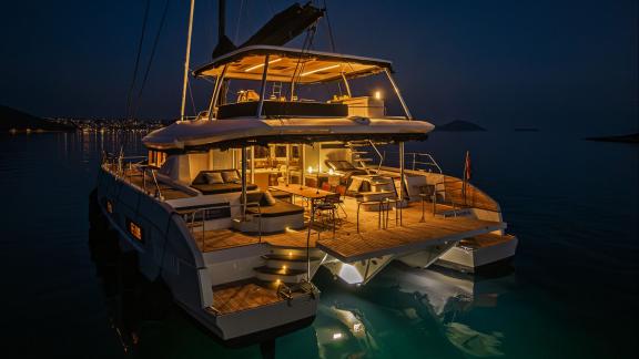 Among catamaran rental options Princess Karla aft deck with lit seating and dining area is seen anchored during evening.