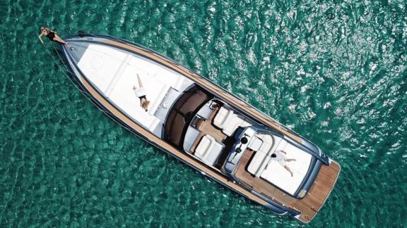 Die Motoryacht Este 2 liegt vor Mykonos im türkisfarbenen Wasser; an Deck genießen Gäste die Sonne.