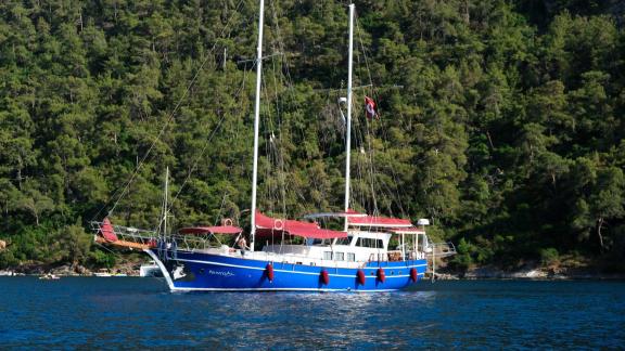 Kırmızı güneş yelkenleri ve Fethiye'nin huzurlu arka planı ile dikkat çeken mavi Gulet Pronto Blue.