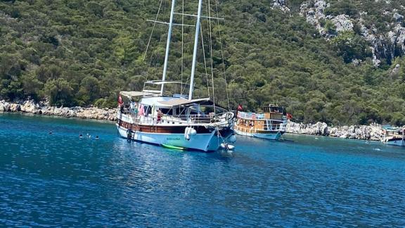 The Queen Almila gulet anchored in a picturesque bay, surrounded by lush nature and clear water.