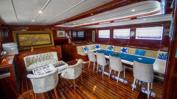 The elegant indoor lounge of the gulet Queen of RTT in Fethiye offers comfortable seating, a large dining table and a ch