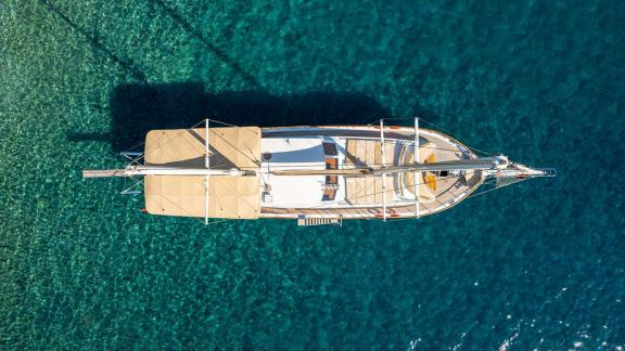 A Bodrum gulet with 5 cabins is photographed from a bird's eye view as it anchors in the clear, turquoise-coloured water