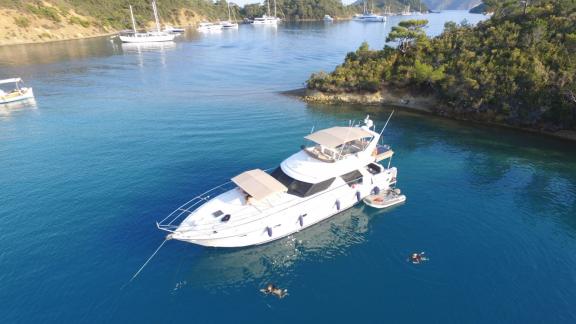 Motor yacht Ayşe Sultan 1 anchored in a bay, people swimming in the water, and other yachts visible around.